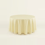 A round tablecloth in a soft cream or ivory color, draped elegantly over a circular table against a seamless, light off-white background.