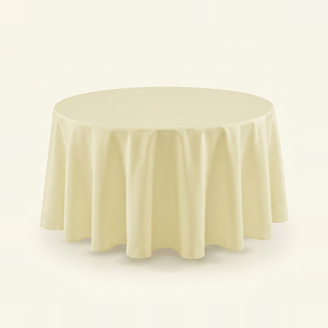 A round tablecloth in a soft cream or ivory color, draped elegantly over a circular table against a solid, light off-white background.