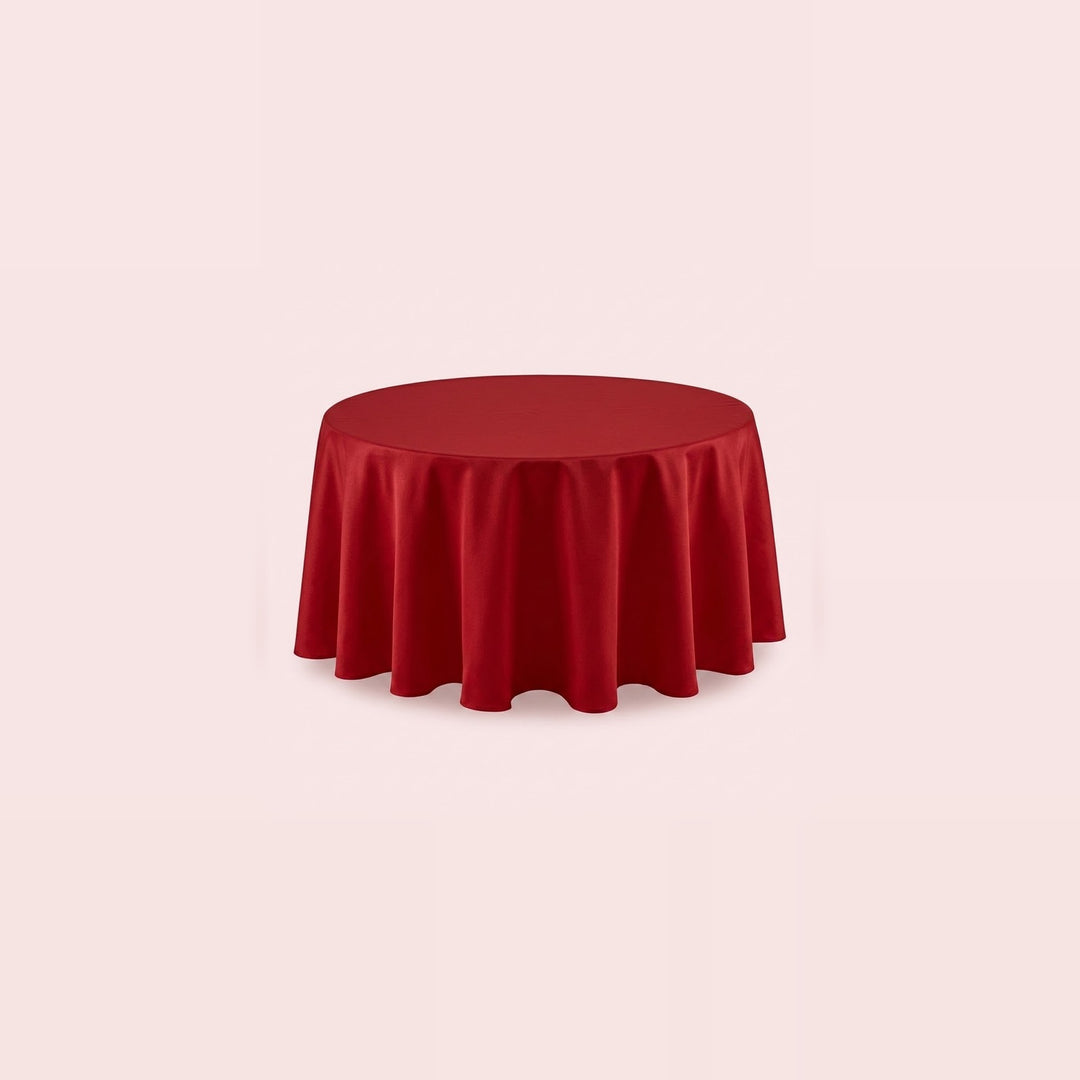 A round red tablecloth draped over a circular table, shown against a solid pale pink background.