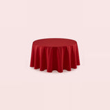 A round red tablecloth draped over a circular table, shown against a solid pale pink background.