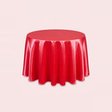 A round red tablecloth with a glossy, satin-like finish, draped over a round table against a solid pale pink background.