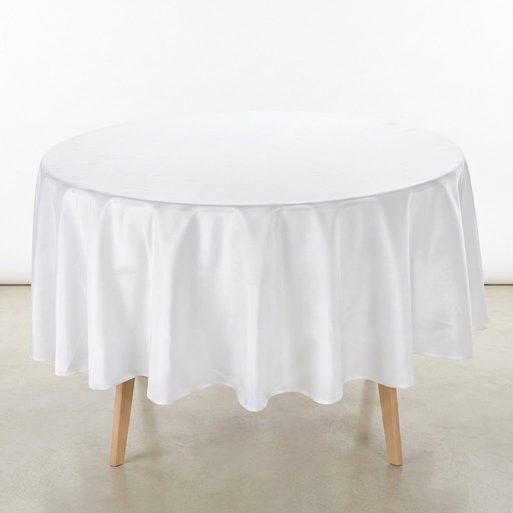 A round white tablecloth draped over a round table with light wood legs, set against a plain white wall and light gray floor.