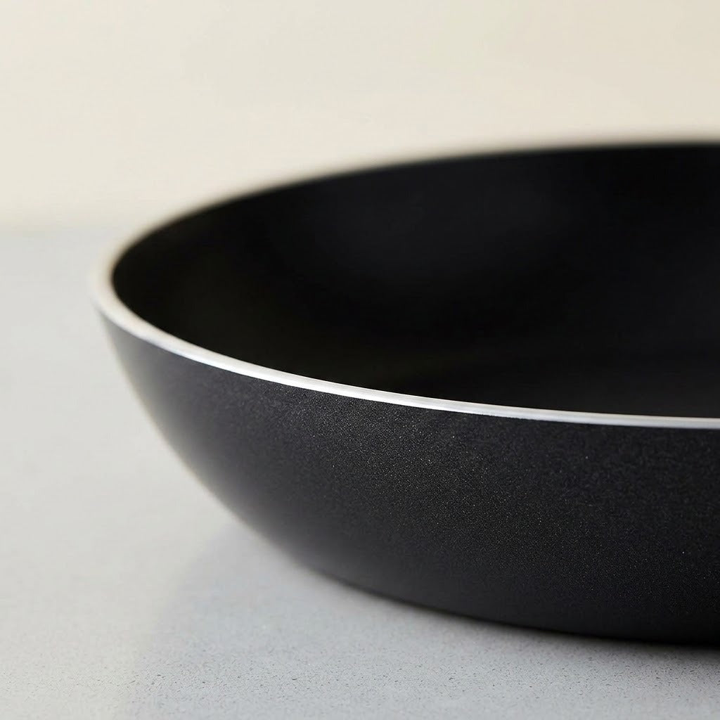 Close-up of a black non-stick frying pan showing the textured exterior and smooth interior, resting on a light gray surface.