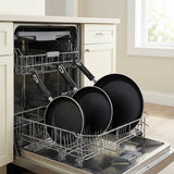 A stainless steel dishwasher with its door open, holding a metal dish rack loaded with black frying pans and plates in a bright kitchen setting.