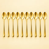 Ten gold disposable spoons stand in a row against a pale gold studio background.