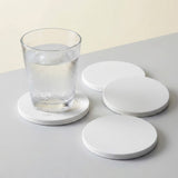 Four round white coasters on a light gray surface, with one coaster holding a clear glass of water.