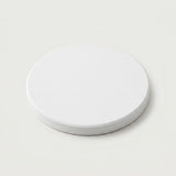A minimalist white circular coaster or tray with a textured top surface and a smooth, slightly darker gray-white rim, shown on a light off-white background.