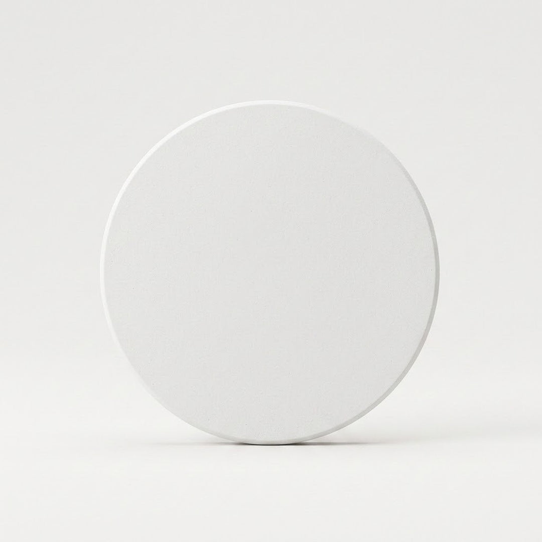 A plain white circular coaster or tile standing upright on a light gray surface against a light gray background.