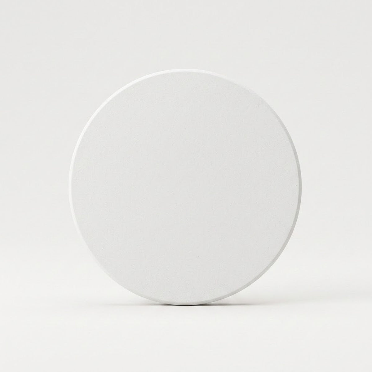 A plain white circular coaster or tile standing upright on a light gray surface against a light gray background.