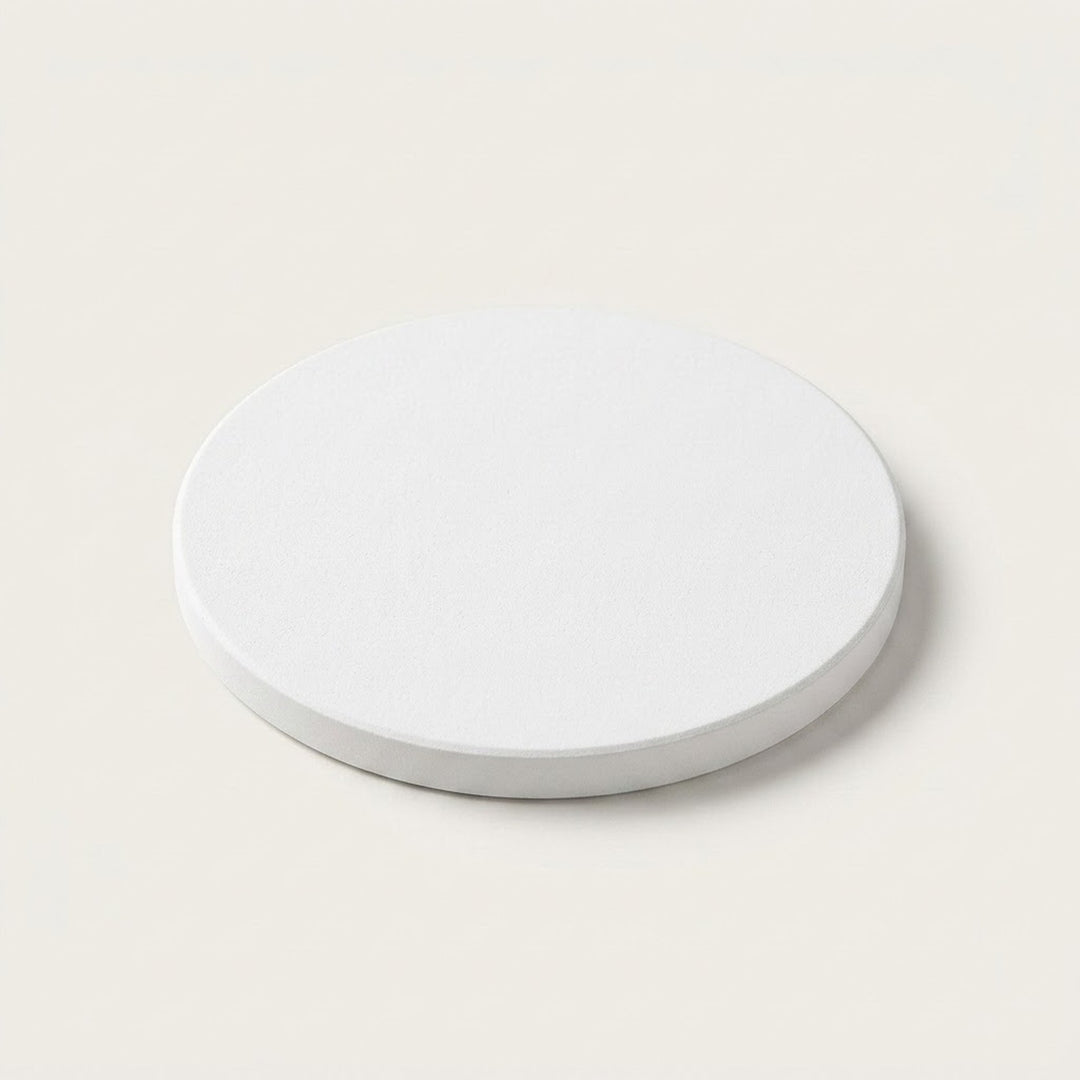 A minimalist round white coaster or tray with a subtle textured surface, shown from a top-down perspective on a solid cream-colored background.
