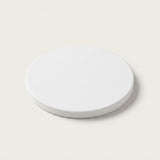 A minimalist round white coaster or tray with a subtle textured surface, shown from a top-down perspective on a solid cream-colored background.