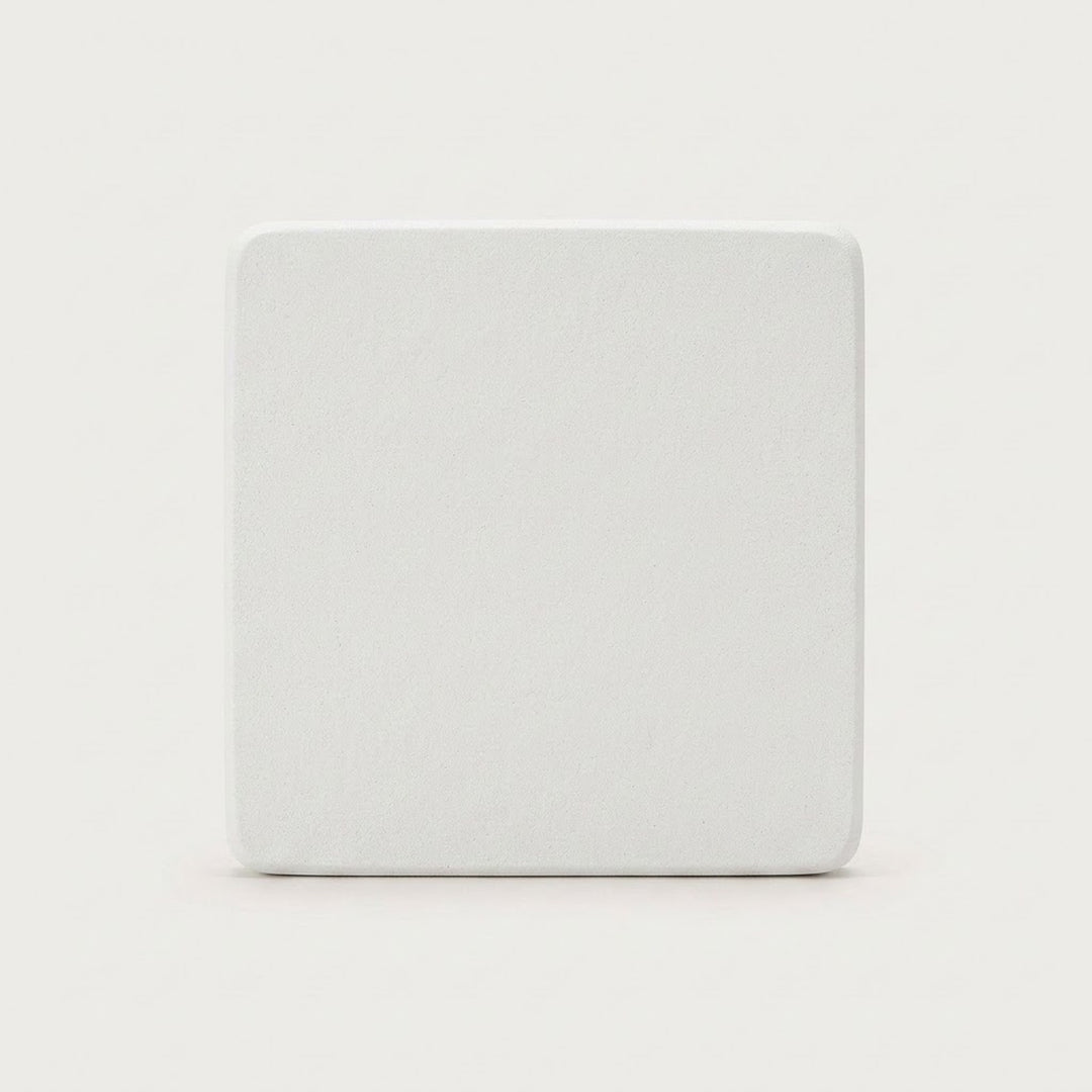 A square white coaster with rounded corners, shown from a top-down view on a light gray background.
