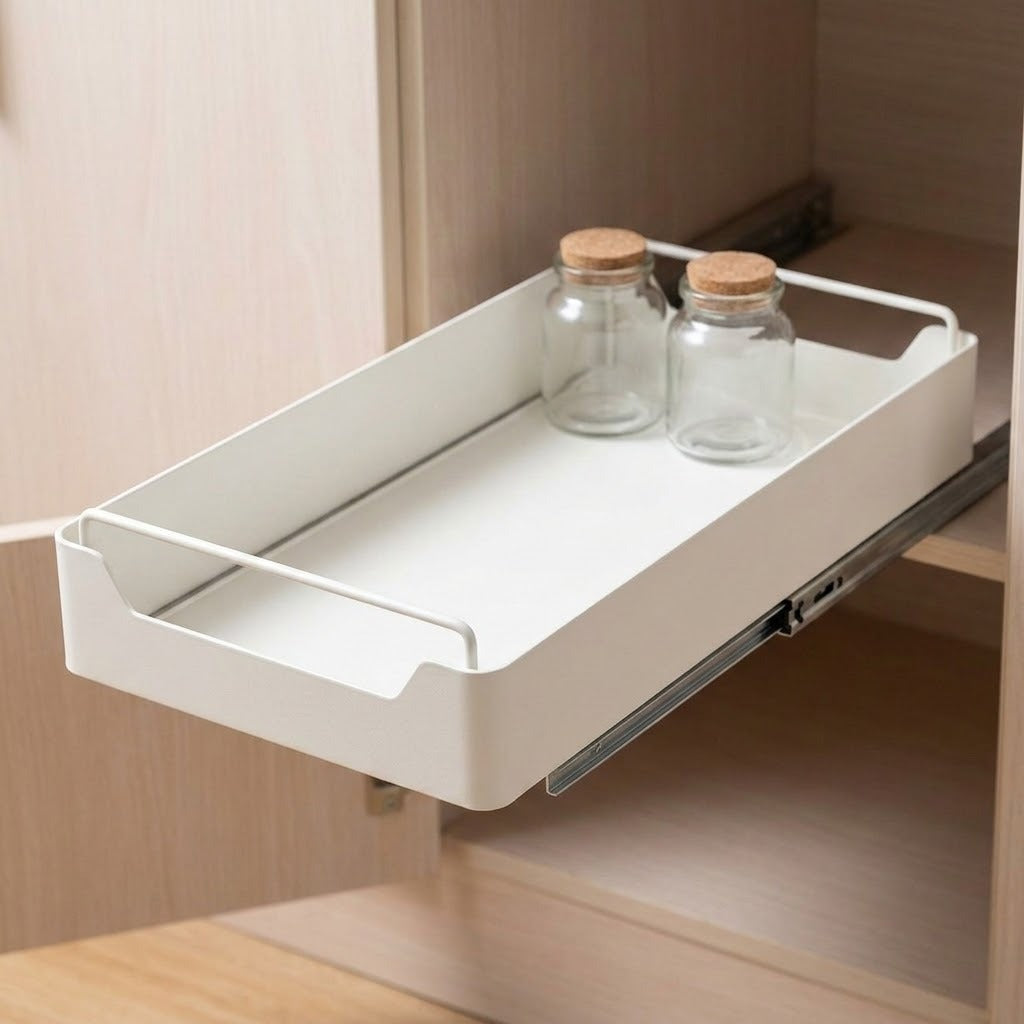 A white pull-out cabinet organizer tray mounted on a sliding drawer inside a light wood cabinet, with two clear glass jars with cork stoppers resting inside.