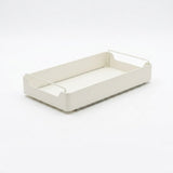 A minimalist rectangular storage tray in a warm off-white/cream color, featuring a flat base and integrated wire side handles, shown on a seamless light gray background.
