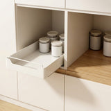 A white pull-out kitchen organizer tray is shown partially extended inside a white cabinet, holding several white canisters with beige lids. A wood countertop is visible in the background.