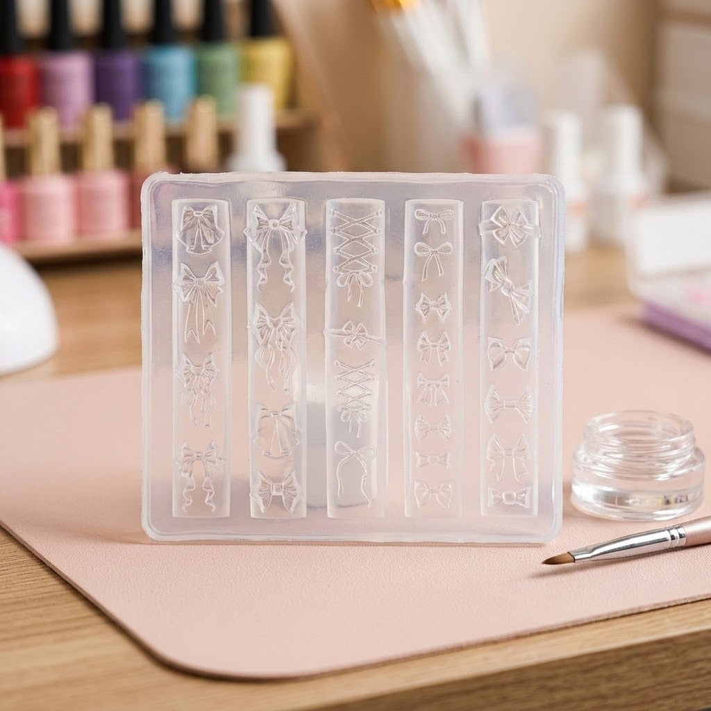 A clear plastic nail stamping mold with five vertical slots featuring bow and floral designs, displayed on a pink mat on a wooden desk with nail supplies in the background.
