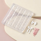 A clear plastic nail art stamping tray with floral and bow designs, shown on a beige and pink background with small white and pink ribbon sample pieces beside it.