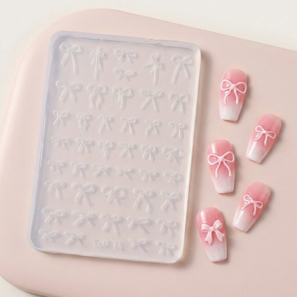 A clear silicone nail stamping tray with embossed bow patterns, shown next to four false nails decorated with pink and white ombre gradients and white bow designs, all on a soft pink background.
