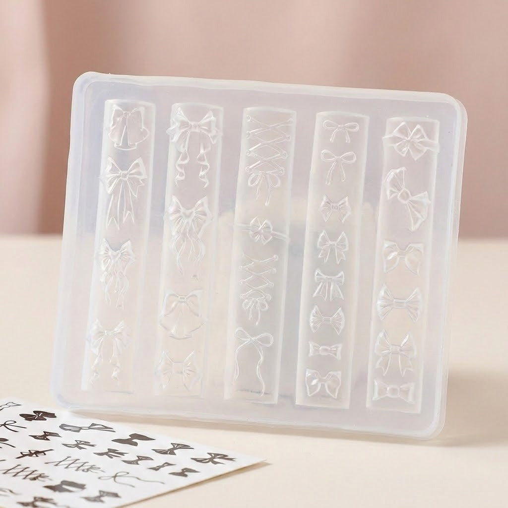 A translucent silicone nail stamping tray with five vertical slots, each molded with different ribbon and bow designs, shown on a light beige surface with a sheet of matching nail stickers in the foreground.