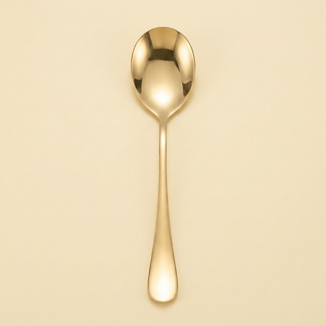 A single polished gold spoon with a reflective finish, centered vertically against a solid, warm cream-colored background.