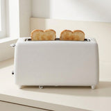 A white two-slot toaster on a light cream countertop, with two slices of toasted bread popping out from the top. The scene is brightly lit with soft natural light from a nearby window.