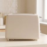 A cream-colored two-slice toaster sits on a white countertop in a bright, softly blurred kitchen setting.