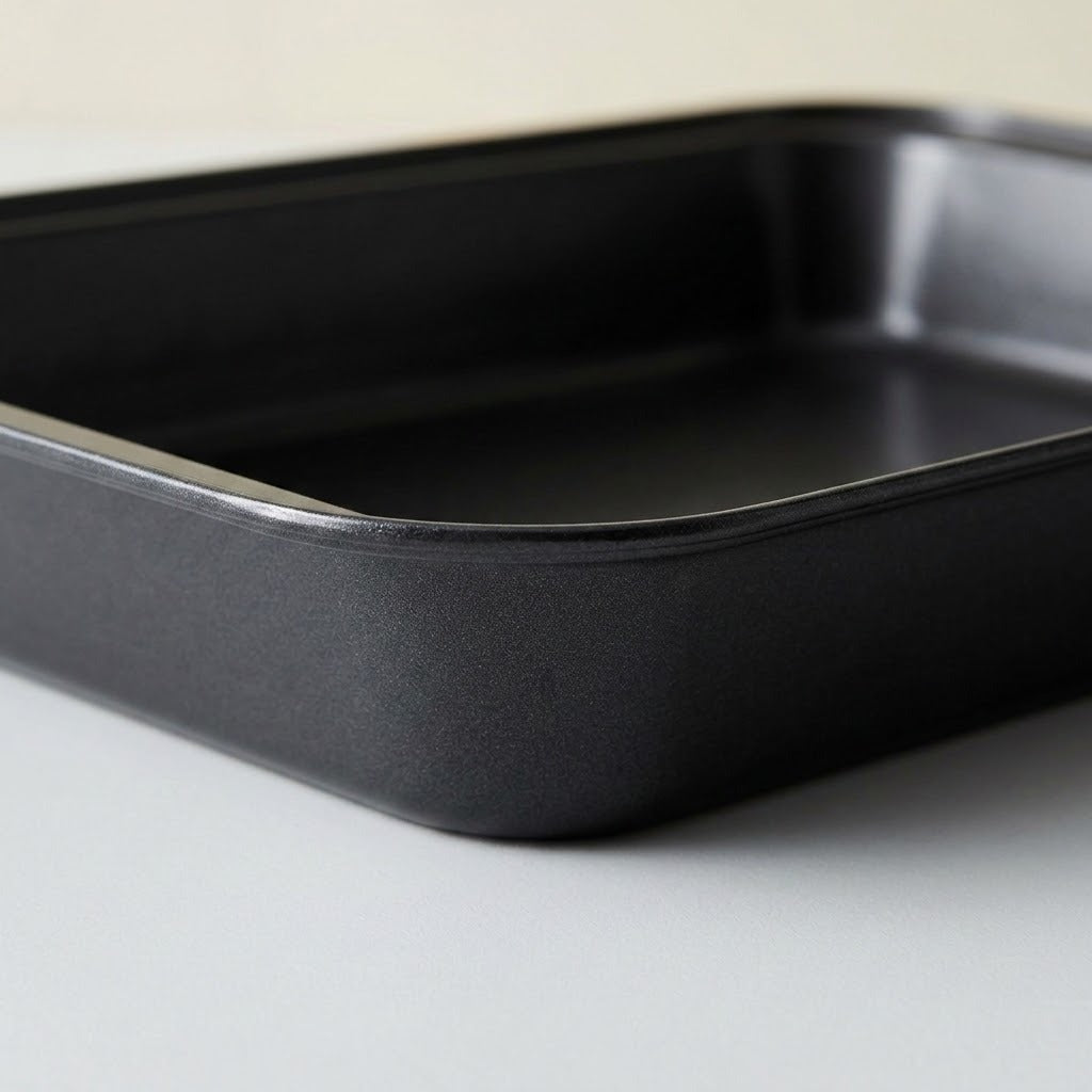 A black rectangular baking pan with rounded corners, photographed on a light gray surface against a neutral off-white background.