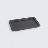 A rectangular black baking tray with raised edges, photographed at an angle on a light gray background.