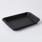 A rectangular black non-stick baking pan with raised rimmed edges, photographed on a clean light gray studio background.