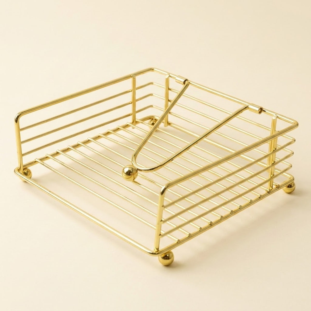 A gold-finished metal wire organizer tray with a slatted base and curved top bars, shown on a plain warm beige background.