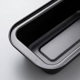 A close-up of a black rectangular baking pan with rounded corners, showing the interior and raised rim on a light gray background.