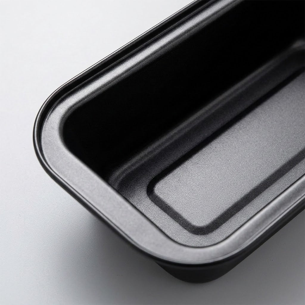 A close-up of a black rectangular baking pan with rounded corners, showing the interior and raised rim on a light gray background.