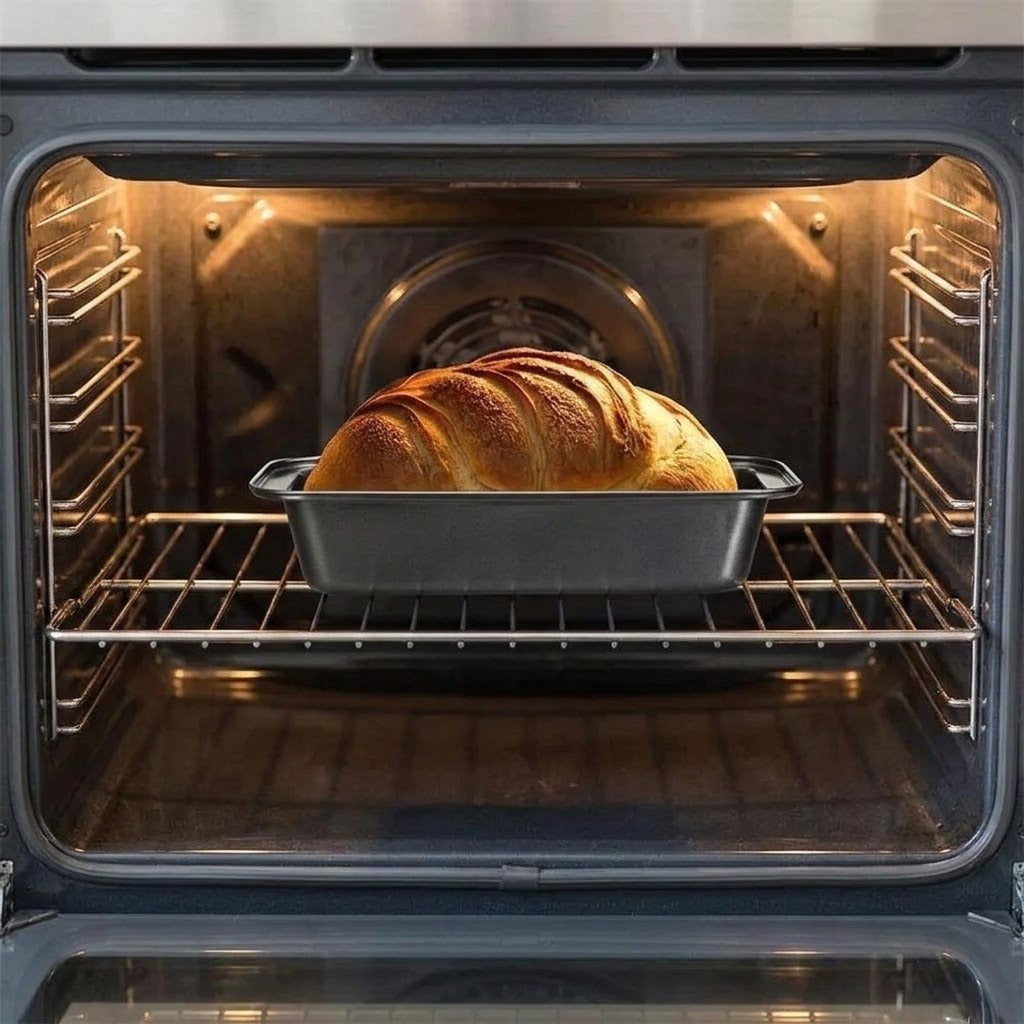 A golden-brown loaf of bread baking on a metal rack inside an open oven.