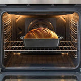 A golden-brown loaf of bread baking on a metal rack inside an open oven.