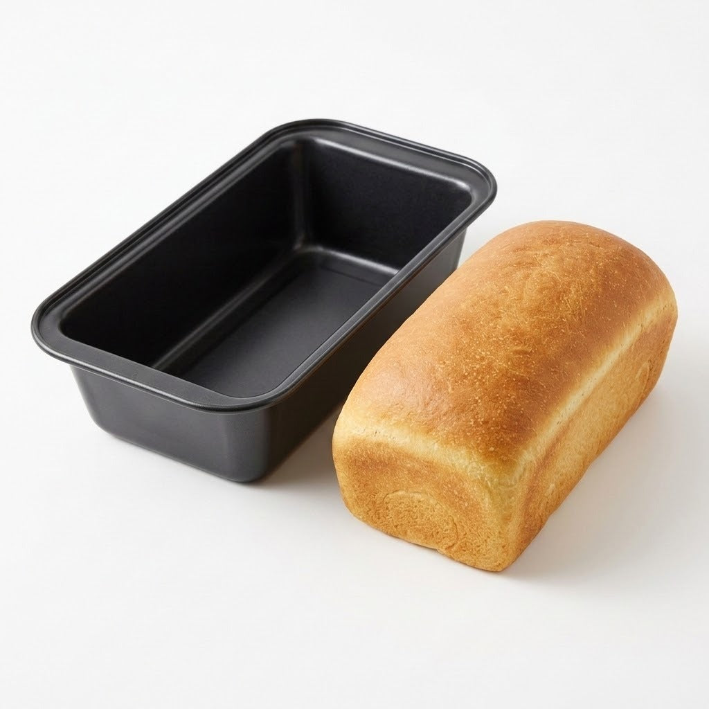 A black rectangular loaf pan shown empty next to a golden-brown baked loaf of bread on a clean white background.