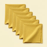 Five folded mustard yellow cloth napkins arranged in a staggered diagonal stack on a light cream background.