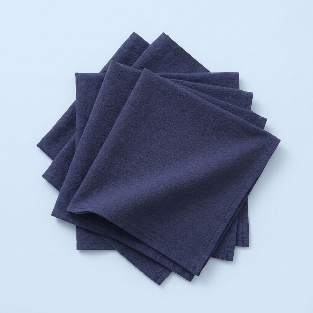 A stack of four dark navy blue square napkins on a light blue background.