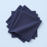 A stack of four dark navy blue square napkins on a light blue background.