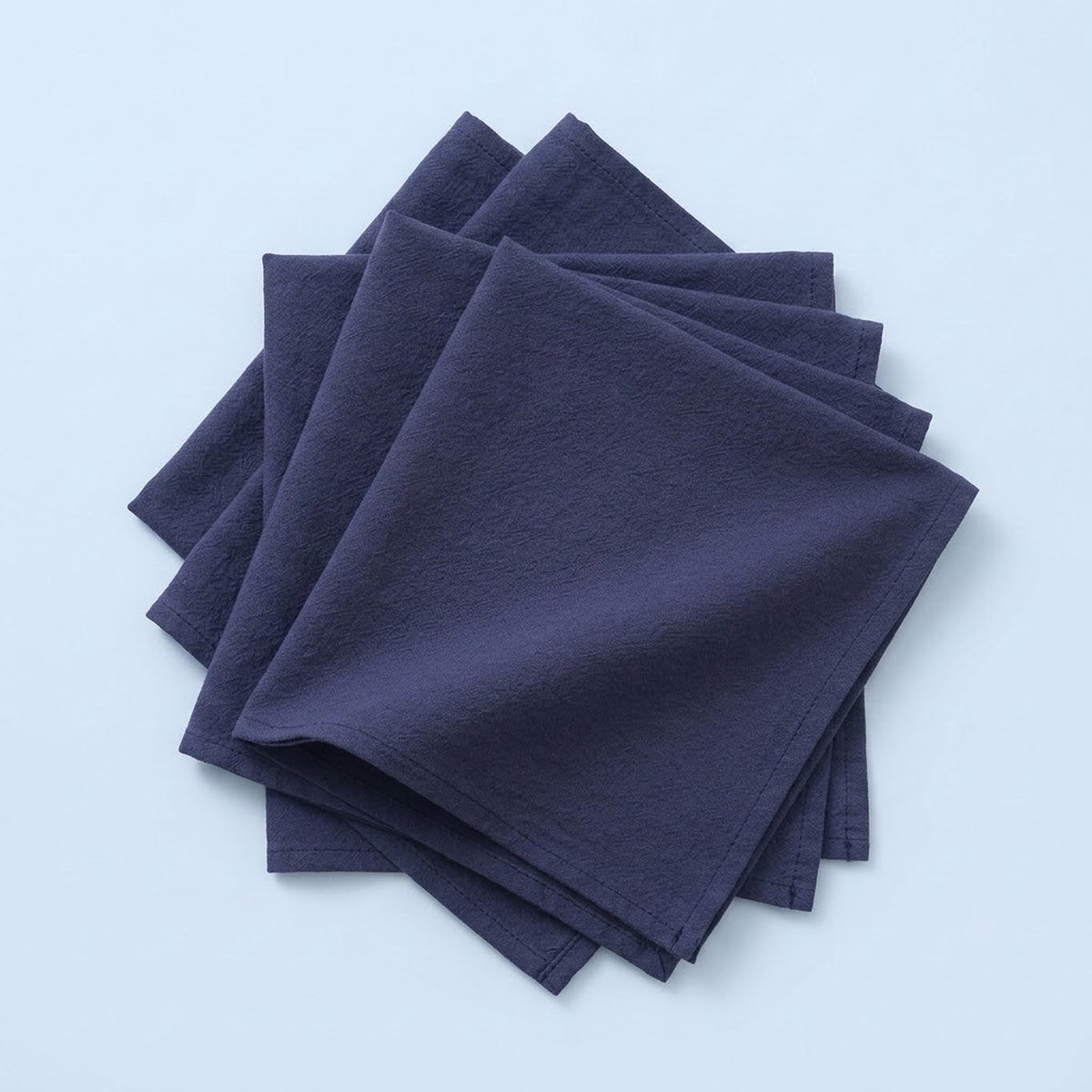 A stack of four dark navy blue square napkins on a light blue background.