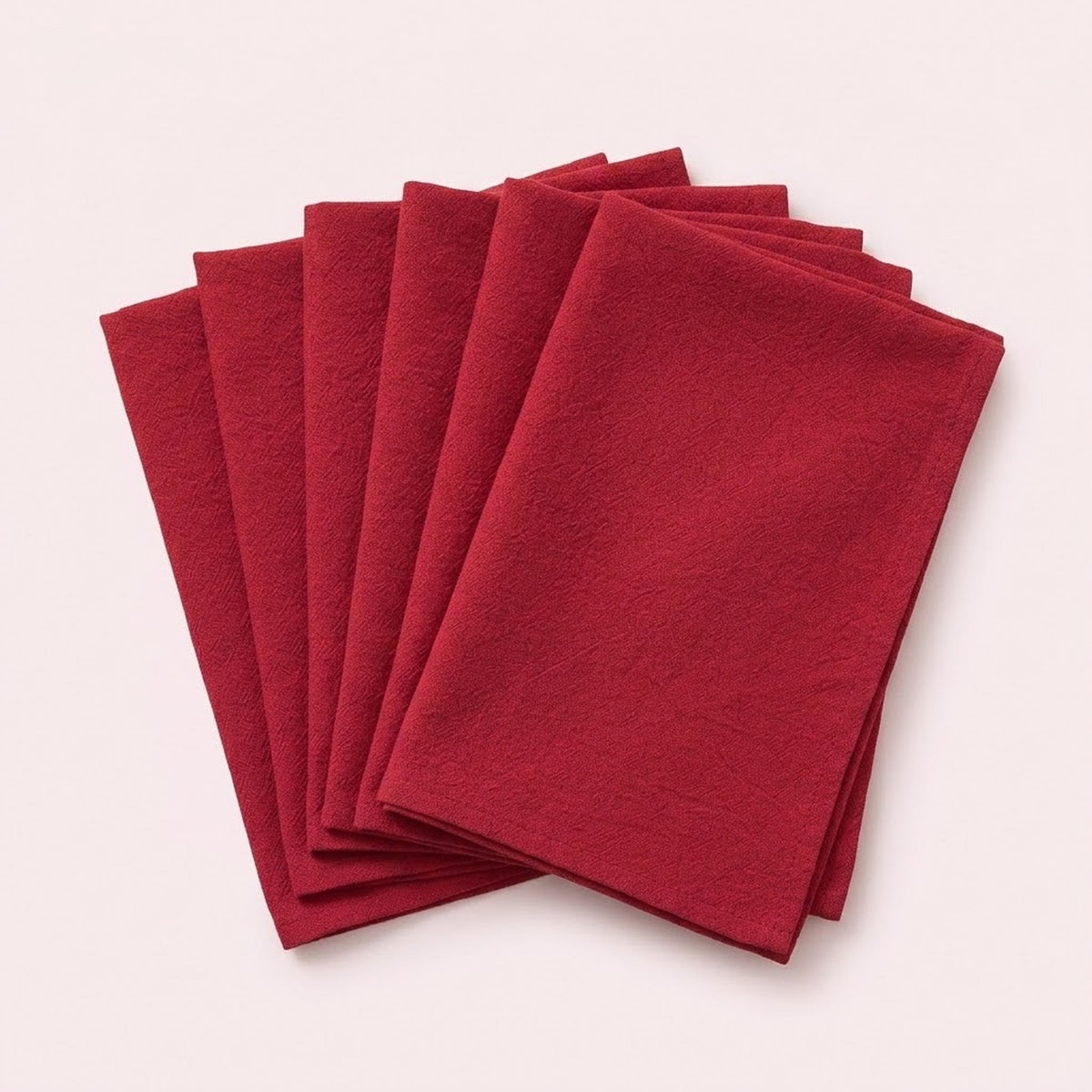 A stack of six folded red fabric napkins arranged in a fan shape on a light beige background.