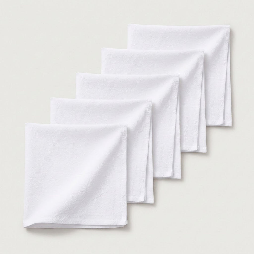 Four white folded cloth napkins arranged in a staggered diagonal stack on a light beige background.