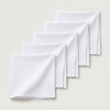Four white folded cloth napkins arranged in a staggered diagonal stack on a light beige background.