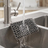 A stainless steel mesh cleaning sponge hanging over a sink with water running from a modern faucet.