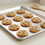 A metal baking sheet holding multiple chocolate chip cookies on a light countertop, with a wooden spoon blurred in the background.