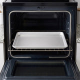 A silver metal baking sheet resting on the middle rack of an open black oven.