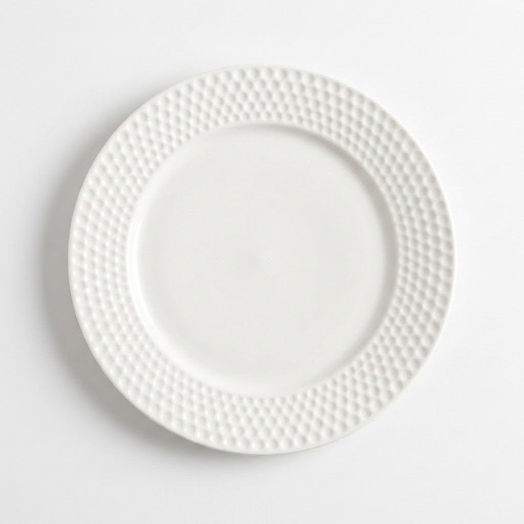 A white ceramic dinner plate with a textured, dimpled border, photographed from directly above on a clean white background.