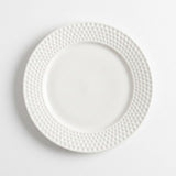 A white ceramic dinner plate with a textured, dimpled border, photographed from directly above on a clean white background.