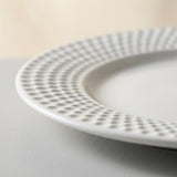 Close-up of a white ceramic plate with a textured, dimpled border pattern, resting on a neutral gray surface.