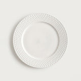 A white ceramic plate with a textured, dimpled border, shown from a top-down view against a light gray background.