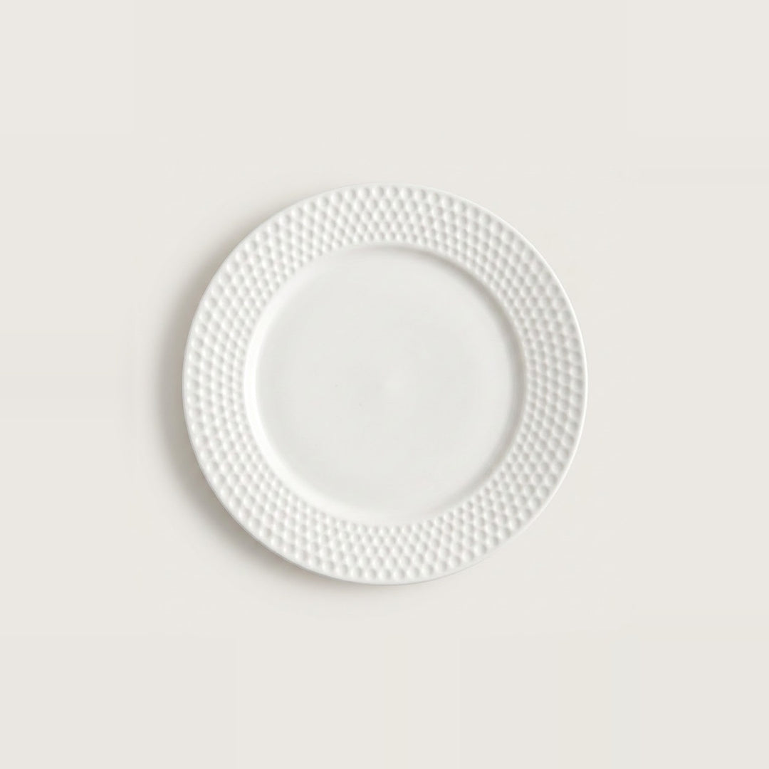 A white ceramic plate with a textured, dimpled pattern around the rim, centered on a light beige background.
